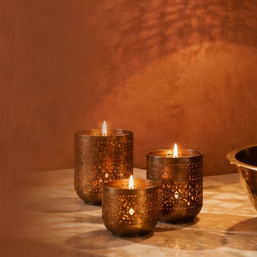 Set of three pierced brass candle votives with lit candles